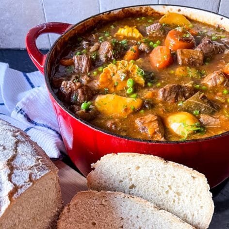 Guinness beef stew in a red Dutch oven with chunks of beef, carrots, corn, peas, and potatoes in a rich sauce, served with crusty bread.