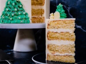 A slice of festive Coconut Almond Cake with layers of almond mascarpone buttercream, decorated with green buttercream Christmas trees.
