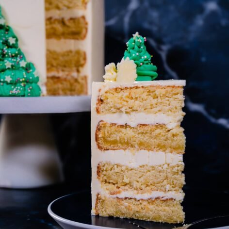 A slice of festive Coconut Almond Cake with layers of almond mascarpone buttercream, decorated with green buttercream Christmas trees.