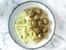 A plate of creamy meatballs in rich sauce, served with fluffy mashed potatoes and garnished with fresh chives, on a marble background.