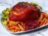 Honey-Dijon glazed ham served with roasted carrots, Brussels sprouts, and cranberry sauce on a white platter.