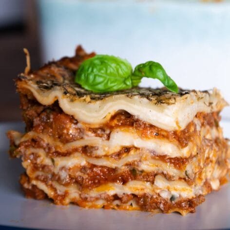A perfectly layered slice of lasagna with fresh pasta, rich meat ragu, creamy béchamel sauce, and a basil garnish on top.