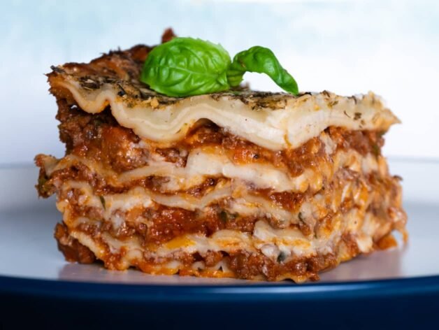 A perfectly layered slice of lasagna with fresh pasta, rich meat ragu, creamy béchamel sauce, and a basil garnish on top.