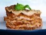 A perfectly layered slice of lasagna with fresh pasta, rich meat ragu, creamy béchamel sauce, and a basil garnish on top.