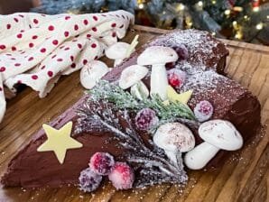 Festive Yule Log dessert with a chocolate sponge, Baileys cream filling, whipped chocolate ganache, and meringue mushrooms on a holiday-themed table.