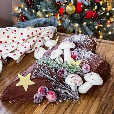 Festive Yule Log dessert with a chocolate sponge, Baileys cream filling, whipped chocolate ganache, and meringue mushrooms on a holiday-themed table.