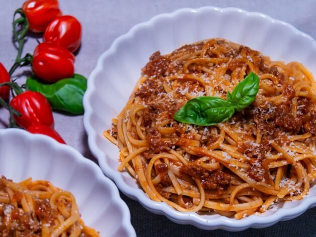 A plate of linguine pasta with Dalmatian-style meat ragu, topped with fresh basil and grated Parmesan cheese.