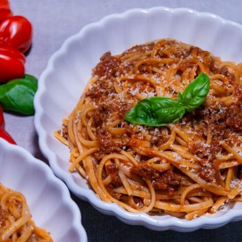 A plate of linguine pasta with Dalmatian-style meat ragu, topped with fresh basil and grated Parmesan cheese.