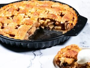 A golden-brown apple pie with a flaky crust, partially sliced to reveal juicy tart apples inside.