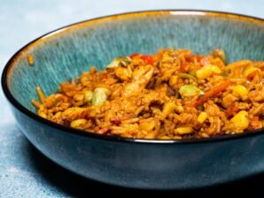 Chicken stir-fry with rice, sweet corn, and vegetables served in a rustic blue bowl.