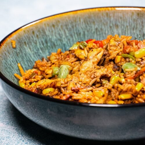 Chicken stir-fry with rice, vegetables, and a savory sauce served in a rustic blue bowl.