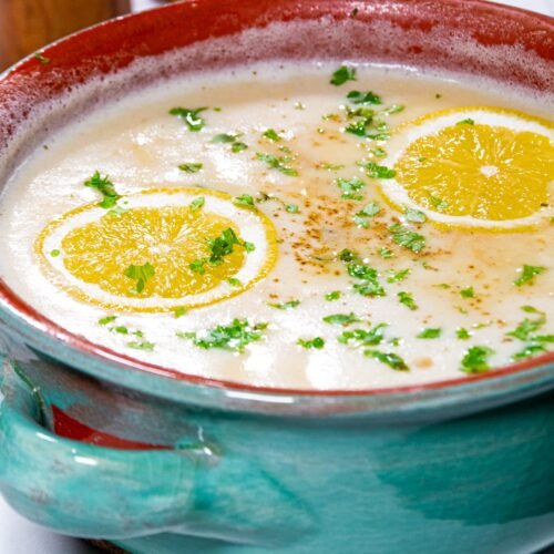 Classic Greek Avgolemono soup garnished with fresh Greek oregano, parsley, and vibrant lemon slices.