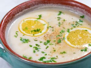 Classic Greek Avgolemono soup garnished with fresh Greek oregano, parsley, and vibrant lemon slices.