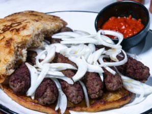 Cevapi served on toasted flatbread with onions, showing a bite taken out of the bread.