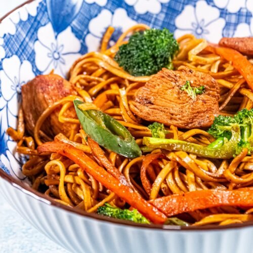 Chicken stir-fry with egg noodles, broccoli, carrots, and black bean sauce in a blue floral bowl.