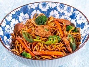 Chicken stir-fry with black bean sauce, egg noodles, broccoli, carrots, and chili peppers served in a blue floral bowl.