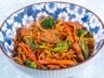 Chicken stir-fry with black bean sauce, egg noodles, broccoli, carrots, and chili peppers served in a blue floral bowl.