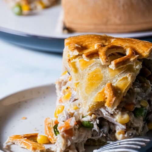 Slice of creamy chicken and mushroom pie with a golden flaky crust, filled with vegetables like corn, peas, and carrots.
