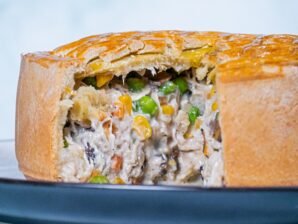 Close-up of a creamy chicken and mushroom pie with a golden crust, showing its rich filling of chicken, mushrooms, corn, and peas.