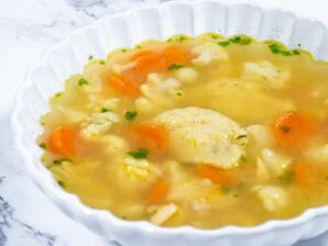 Bowl of Chicken Semolina Dumpling Soup with carrots, cauliflower, and parsley garnish.