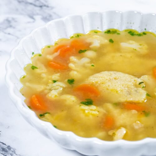 Close-up of Chicken Semolina Dumpling Soup showing fluffy dumplings and fresh vegetables.