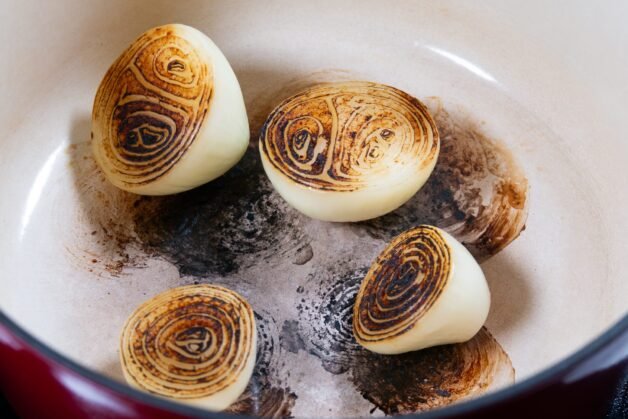 Charred onion halves in a pot for chicken stock preparation.