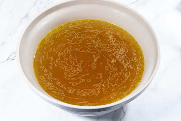 Strained chicken stock in a bowl with golden color.