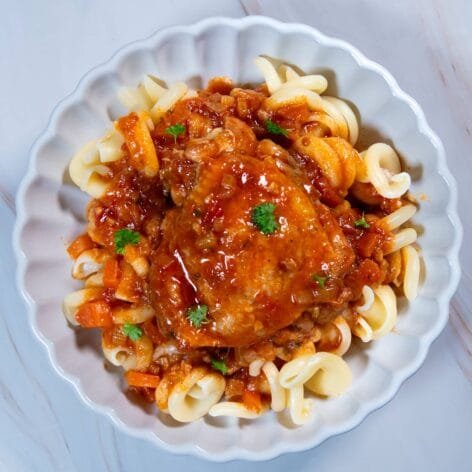 Chicken in tomato sauce served over pasta, garnished with fresh parsley.