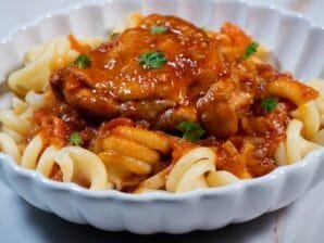 Close-up of chicken in tomato sauce served over pasta, garnished with parsley.