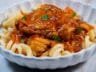 Close-up of chicken in tomato sauce served over pasta, garnished with parsley.