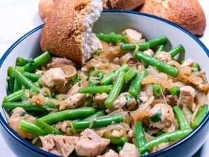A bowl of chicken with green beans and caramelized onions served with crusty bread.
