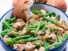 A bowl of chicken with green beans and caramelized onions served with crusty bread.