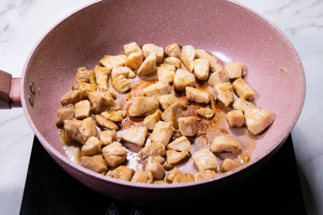 Chicken cubes searing in a pink skillet until golden brown.