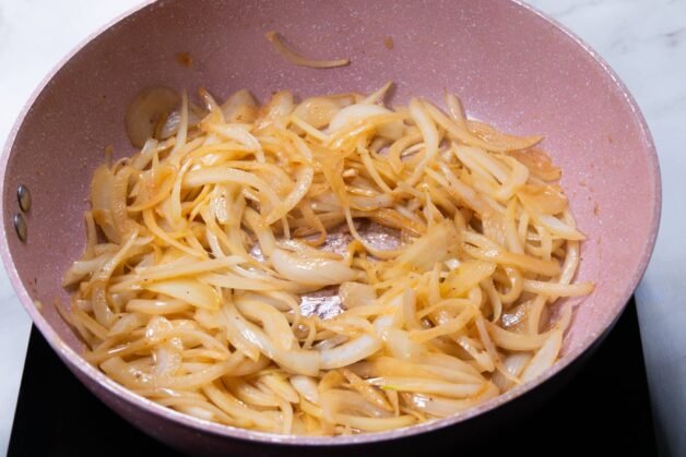 Sliced onions caramelizing in a skillet with butter and olive oil.