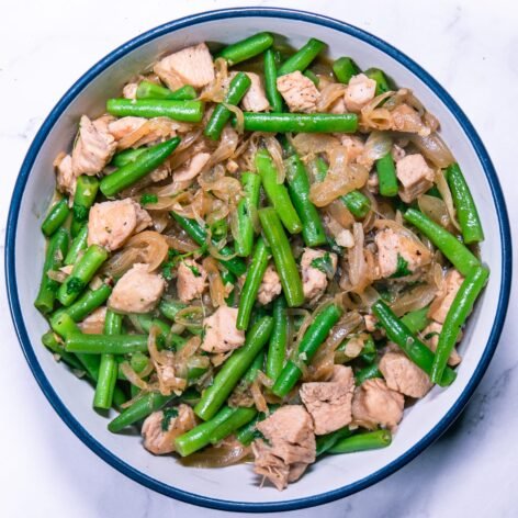 An overhead view of chicken with green beans and caramelized onions in a white and blue bowl.