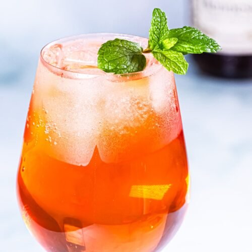 A vibrant Citrus Hennessy Spritz cocktail served in a large glass, garnished with fresh mint leaves, against a light background.