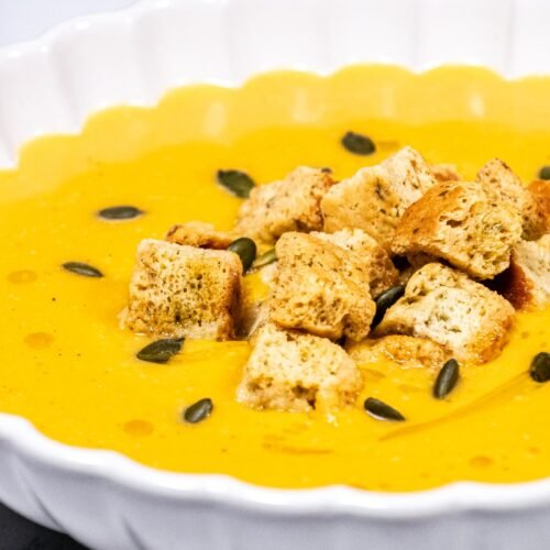 A bowl of creamy butternut squash soup topped with crunchy croutons, toasted pumpkin seeds, and a drizzle of olive oil.