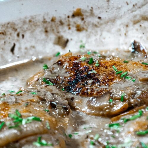 Close-up of crispy, golden chicken thighs simmered in a creamy mushroom and leek sauce with fresh chive garnish.
