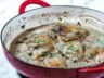 Golden brown chicken thighs simmered in a creamy mushroom and leek sauce, garnished with fresh herbs in a red skillet.