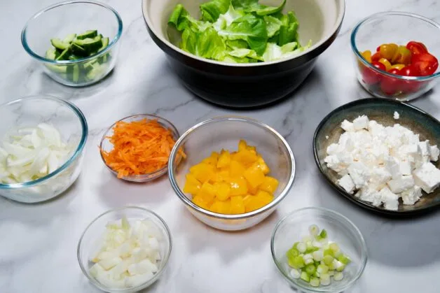 Prepared vegetables in bowls for assembling a fresh salad.