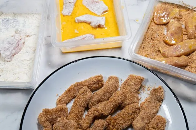 Process of breading chicken with flour, egg, and breadcrumbs in separate bowls.