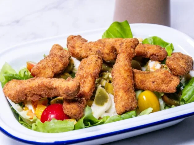 Crispy chicken strips arranged on top of a colorful salad in a white dish.