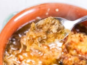 A spoonful of French onion soup with caramelized onions and melted cheese.