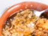 A spoonful of French onion soup with caramelized onions and melted cheese.