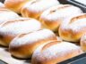 Fluffy Greek yogurt buns dusted with powdered sugar, freshly baked on a parchment-lined tray.