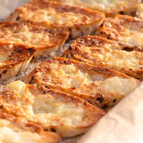 Golden garlic bread slices on a baking sheet with melted cheese topping.