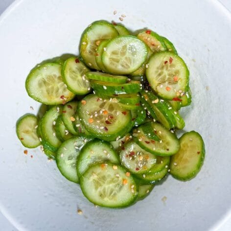 Korean cucumber salad (Oi Muchim) in a white bowl, garnished with sesame seeds and chili flakes.