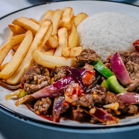 A plated serving of Lomo Saltado with beef, stir-fried vegetables, French fries, and a side of white rice.