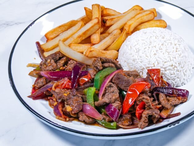 A plated serving of Lomo Saltado with beef, stir-fried vegetables, French fries, and a side of white rice.