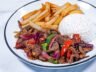 A plated serving of Lomo Saltado with beef, stir-fried vegetables, French fries, and a side of white rice.